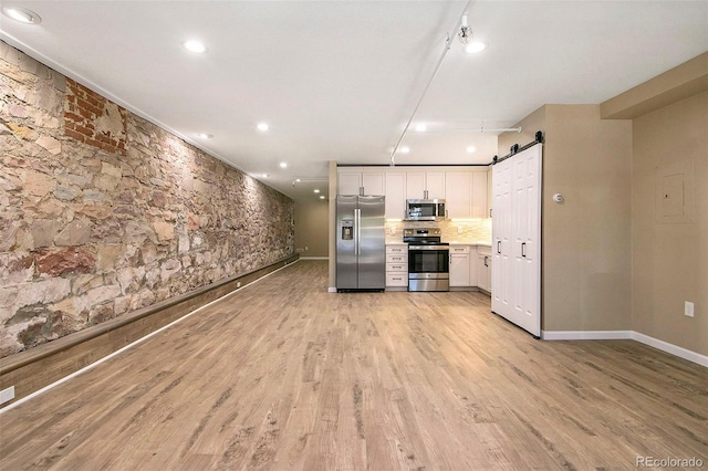 kitchen with light wood finished floors, stainless steel appliances, decorative backsplash, white cabinets, and a barn door