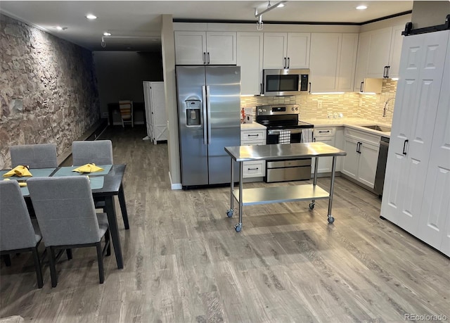 kitchen with appliances with stainless steel finishes, white cabinetry, sink, a barn door, and light wood-type flooring