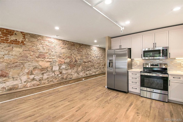 kitchen featuring backsplash, light countertops, light wood-style flooring, white cabinets, and stainless steel appliances