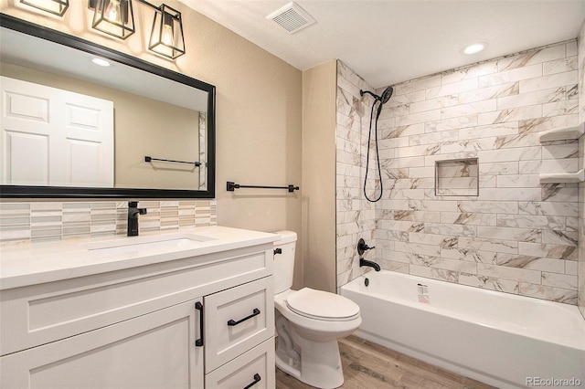 full bathroom featuring tiled shower / bath, wood-type flooring, decorative backsplash, vanity, and toilet