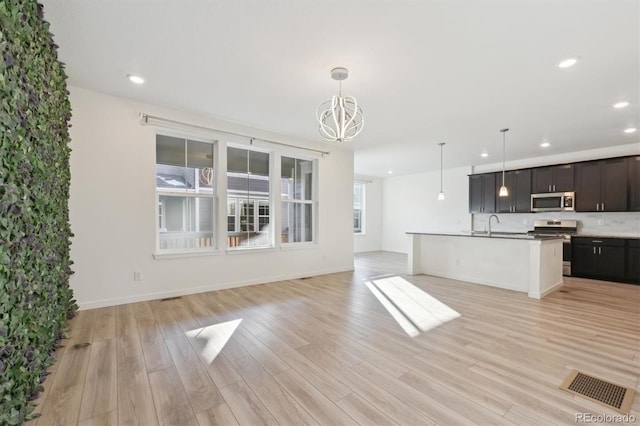 interior space with decorative light fixtures, stainless steel appliances, a center island with sink, and light hardwood / wood-style flooring