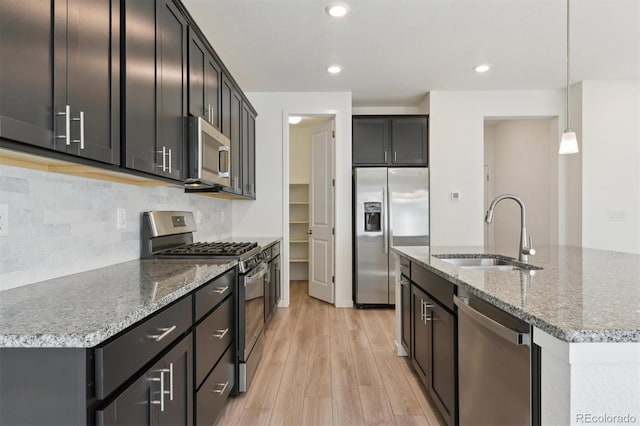 kitchen with a kitchen island with sink, appliances with stainless steel finishes, pendant lighting, and sink