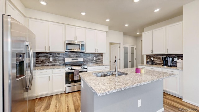 14074 Jackson St, Thornton, CO 80602 - kitchen with appliances with stainless steel finishes, light wood finished floors, decorative backsplash, a center island with sink, and white cabinetry