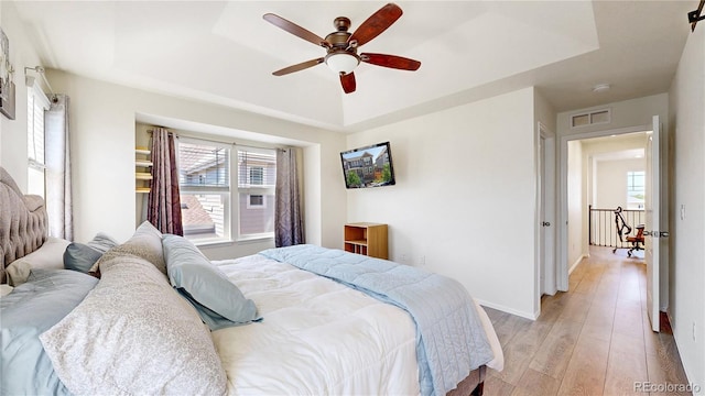 14074 Jackson St, Thornton, CO 80602 - bedroom featuring a tray ceiling, multiple windows, light wood-style flooring, and a ceiling fan