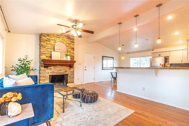 living room featuring lofted ceiling with beams, a fireplace, a ceiling fan, baseboards, and light wood finished floors