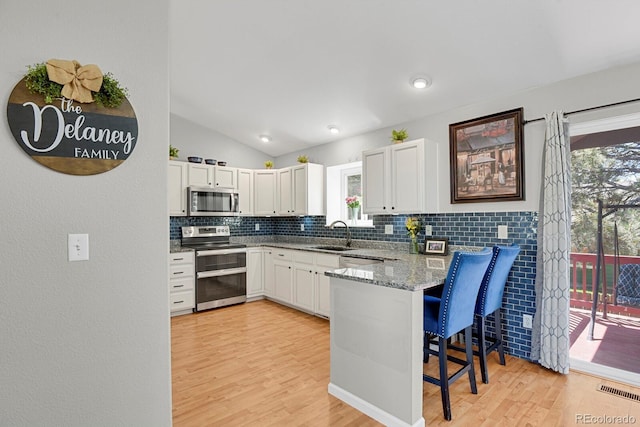 kitchen with stainless steel appliances, tasteful backsplash, a breakfast bar, a sink, and light wood-type flooring