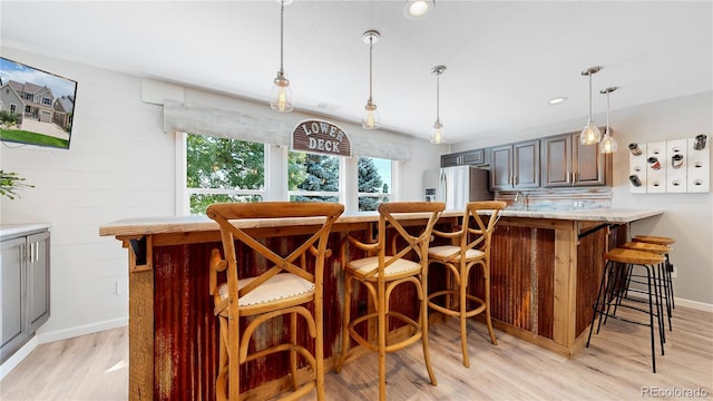 bar featuring stainless steel refrigerator with ice dispenser, light stone countertops, light hardwood / wood-style floors, and pendant lighting