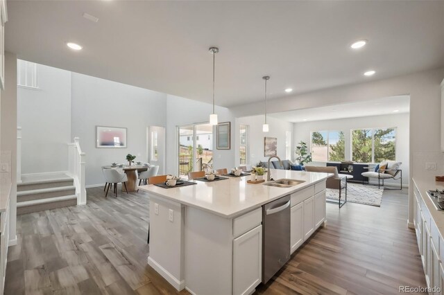 kitchen featuring light wood-type flooring, stainless steel dishwasher, pendant lighting, white cabinetry, and an island with sink