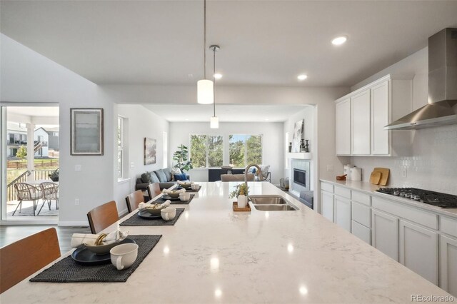 kitchen with sink, wall chimney exhaust hood, stainless steel gas cooktop, a kitchen breakfast bar, and white cabinets