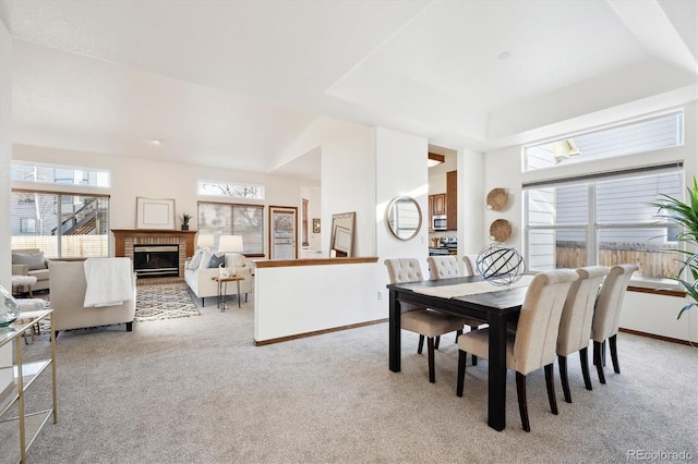 dining area with a raised ceiling, light colored carpet, and a brick fireplace