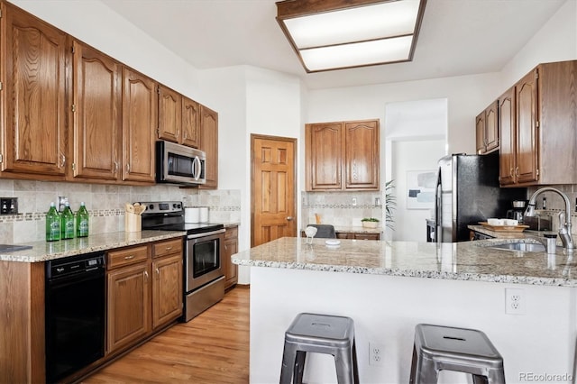 11144 Navajo St, Northglenn, CO 80234 - kitchen featuring stainless steel appliances, a peninsula, a kitchen breakfast bar, light stone countertops, and light wood-style flooring