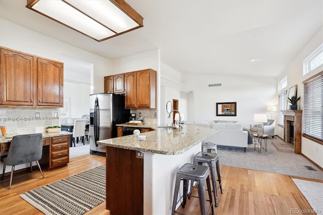 kitchen with light stone counters, light hardwood / wood-style flooring, stainless steel refrigerator with ice dispenser, kitchen peninsula, and a breakfast bar area