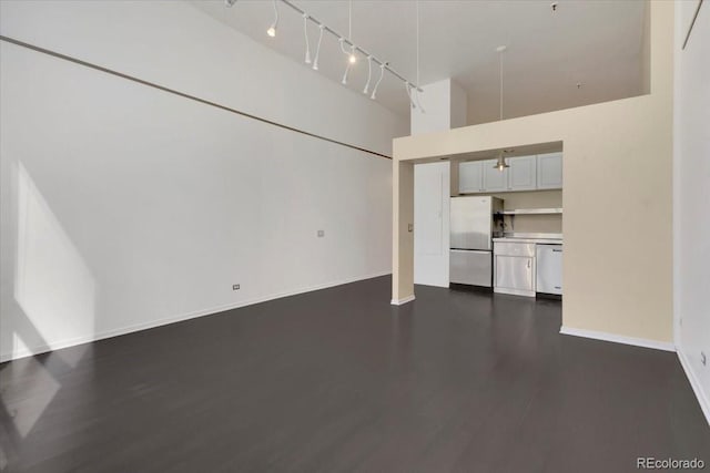 unfurnished living room with a high ceiling, baseboards, track lighting, and dark wood-style flooring