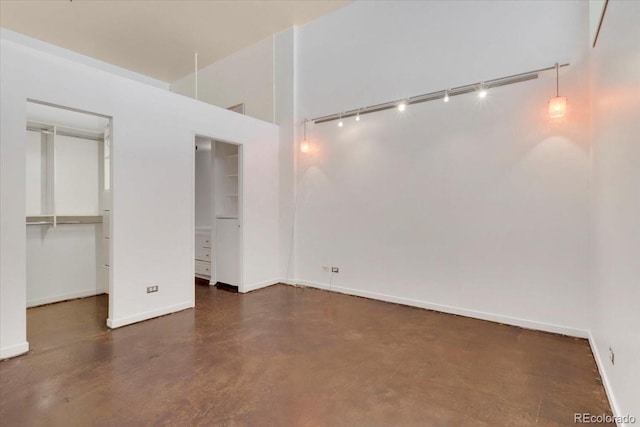 unfurnished bedroom with track lighting, baseboards, a walk in closet, and concrete flooring