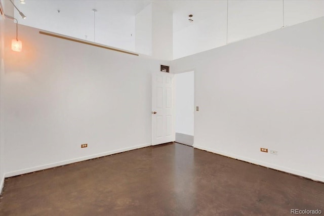 unfurnished room featuring a high ceiling, baseboards, and concrete flooring