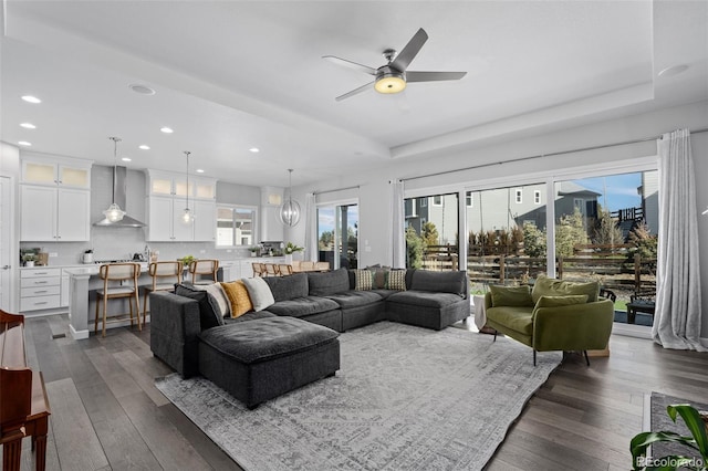 living room featuring a ceiling fan, recessed lighting, a raised ceiling, and dark wood-style flooring