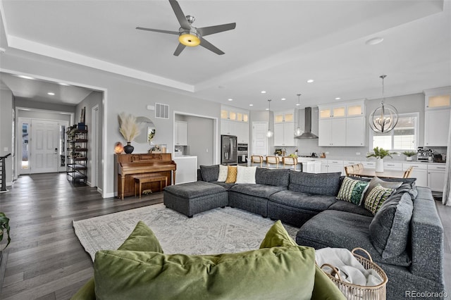 living area with recessed lighting, visible vents, dark wood finished floors, a tray ceiling, and ceiling fan with notable chandelier