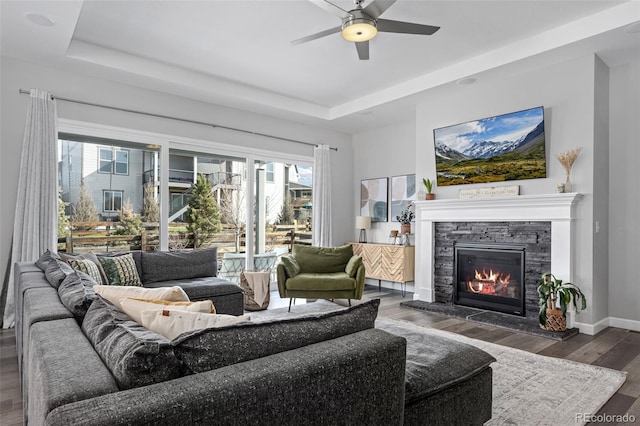 living area with baseboards, a fireplace, a tray ceiling, and wood finished floors