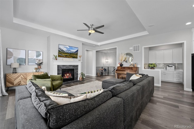 living area with a fireplace with flush hearth, wood finished floors, visible vents, a ceiling fan, and a raised ceiling