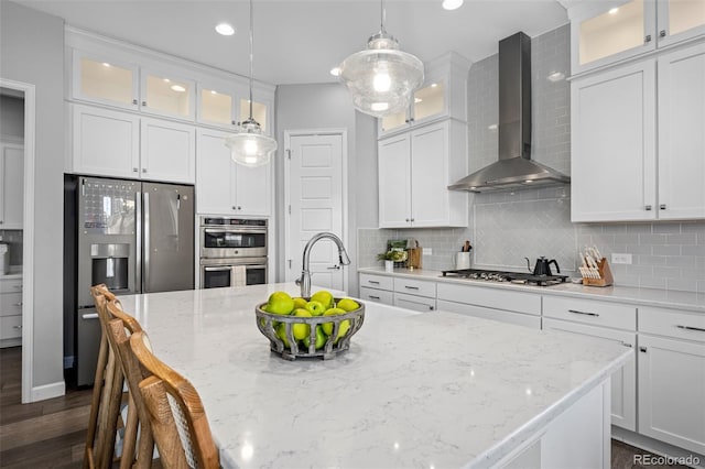 kitchen with appliances with stainless steel finishes, a center island with sink, wall chimney range hood, and tasteful backsplash