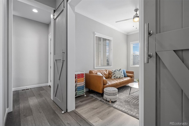 sitting room with a barn door, baseboards, a ceiling fan, wood finished floors, and crown molding