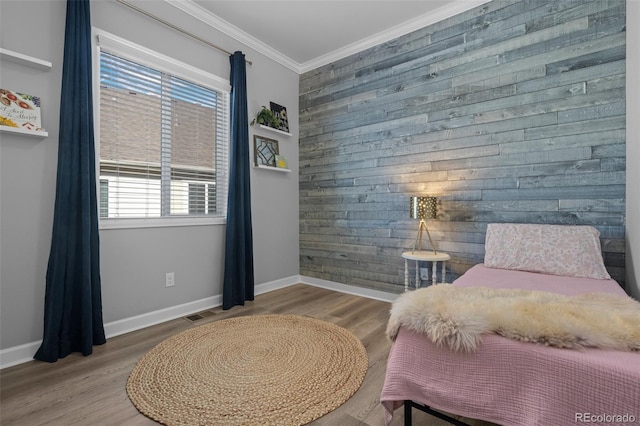 bedroom featuring wood walls, an accent wall, crown molding, and wood finished floors