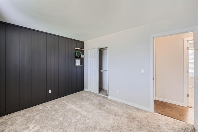 unfurnished bedroom with a closet, baseboards, carpet, and wood walls