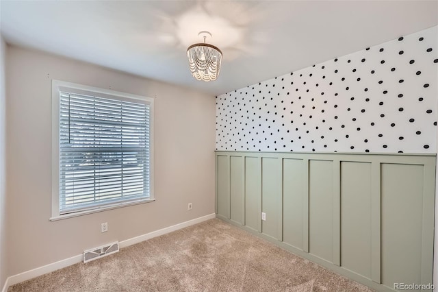 carpeted spare room with visible vents, baseboards, and a chandelier