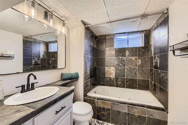 bathroom featuring a drop ceiling, toilet, vanity, and tiled shower / bath