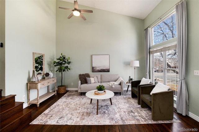 living area with dark wood-type flooring, a ceiling fan, baseboards, and a towering ceiling