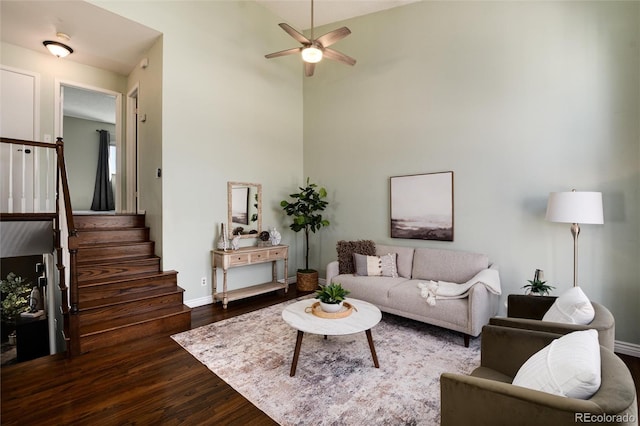 living area featuring baseboards, a ceiling fan, dark wood-style flooring, and stairs