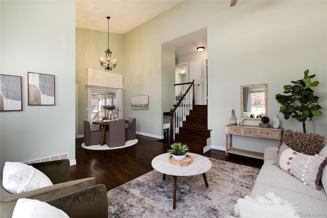 living area with baseboards, stairway, wood finished floors, a towering ceiling, and an inviting chandelier