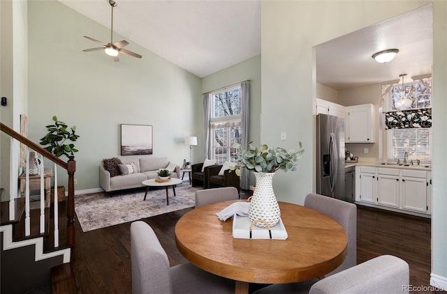 dining area with stairway, ceiling fan with notable chandelier, dark wood-style flooring, and vaulted ceiling