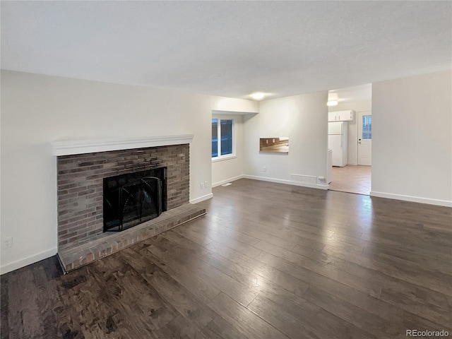 unfurnished living room featuring dark hardwood / wood-style flooring and a brick fireplace