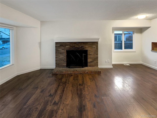 unfurnished living room featuring a textured ceiling, a healthy amount of sunlight, dark hardwood / wood-style flooring, and a fireplace