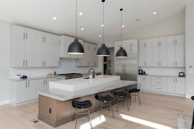 kitchen featuring a kitchen island with sink, sink, white cabinets, and decorative light fixtures