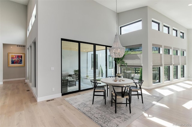 dining room featuring a chandelier, a high ceiling, light wood-type flooring, and a wealth of natural light