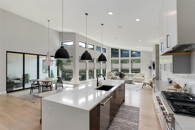 kitchen with sink, decorative light fixtures, white cabinets, plenty of natural light, and an island with sink