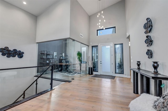 entryway featuring an inviting chandelier, a towering ceiling, and light wood-type flooring