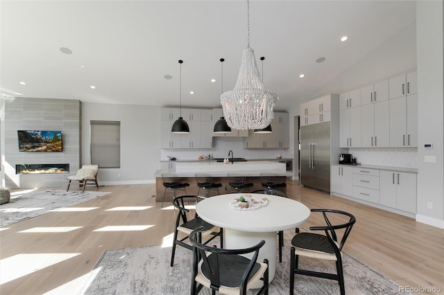 dining space with recessed lighting, light wood-style flooring, a large fireplace, a chandelier, and baseboards