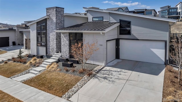 contemporary home with a standing seam roof, metal roof, a garage, stone siding, and driveway