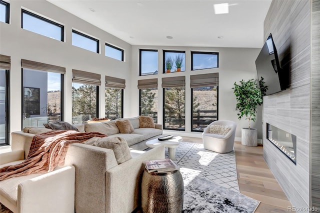 living area featuring a wealth of natural light, a premium fireplace, a towering ceiling, and light wood-style flooring