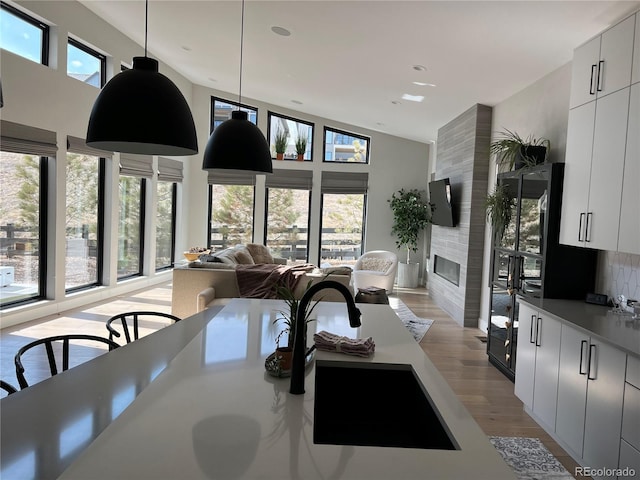 7125 Skygazer St, Castle Pines, CO 80108 - kitchen featuring a fireplace, modern cabinets, light wood-style flooring, a high ceiling, and pendant lighting