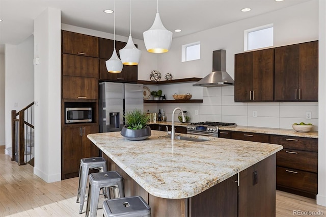 kitchen with tasteful backsplash, stainless steel appliances, a sink, dark brown cabinets, and wall chimney exhaust hood