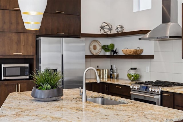 kitchen with dark brown cabinets, appliances with stainless steel finishes, a sink, wall chimney range hood, and backsplash