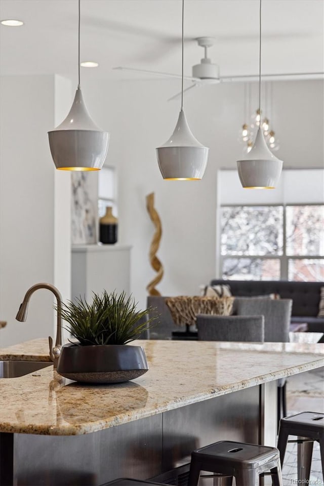 kitchen featuring a kitchen bar, a sink, decorative light fixtures, and light stone counters