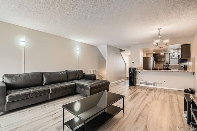 living room featuring a textured ceiling, light wood-type flooring, and a notable chandelier