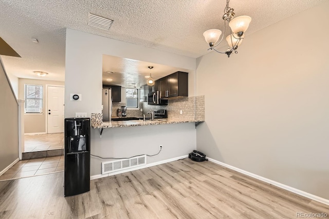 kitchen featuring kitchen peninsula, appliances with stainless steel finishes, backsplash, light stone counters, and decorative light fixtures