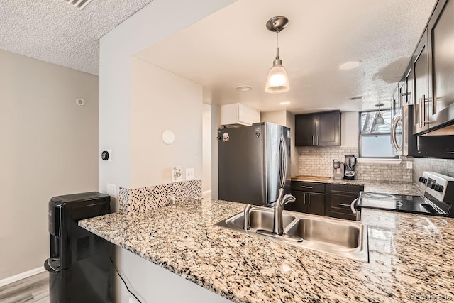 kitchen featuring kitchen peninsula, appliances with stainless steel finishes, decorative light fixtures, and light stone counters