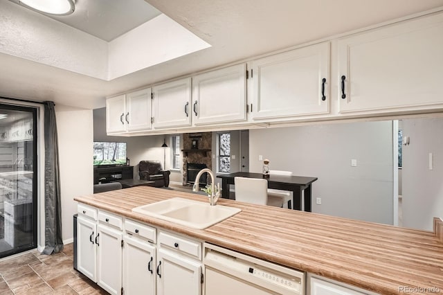 kitchen with white dishwasher, a stone fireplace, a sink, and white cabinetry